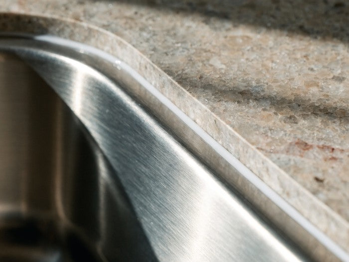 AI shot reference standing in for photography. A kitchen. Sink rim or countertop-to-wall joint with the white bead run and tooled.