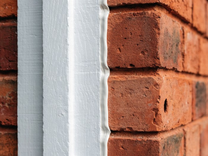 AI shot reference standing in for photography. Exterior. Door frame meeting brick or siding, the cured bead in the joint.