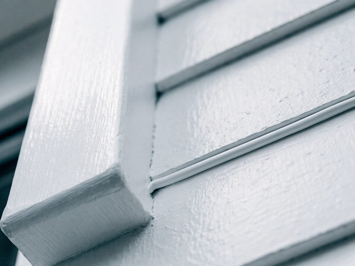 AI shot reference standing in for photography. Exterior, daylight. Window trim meeting siding, white bead tooled along the perimeter.