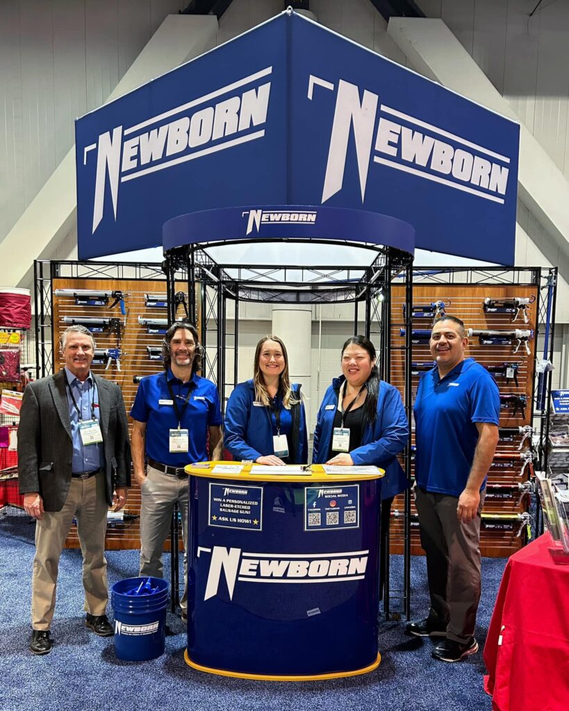 a group of people standing in front of a NewBorn caulk gun booth.